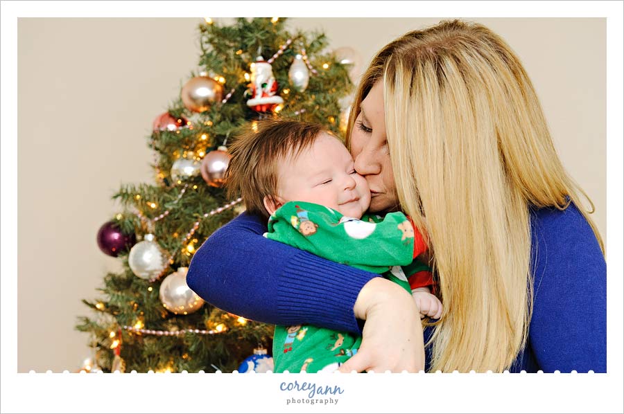 mom kissing baby son in front of christmas tree